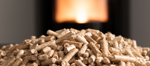 A mound of pellets in the foreground in front of a blurred lit pellet stove in the background.